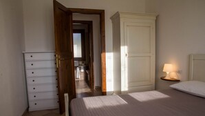 A bedroom with a bed, a dresser, a wardrobe, and a nightstand with a lamp. - GF Apartments La Vigna - Vigna Superior - LEVANTE (BADESI)
