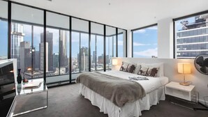 Quarto moderno com vista para a cidade, uma cama grande, mesas de cabeceira e uma escrivaninha de vidro.