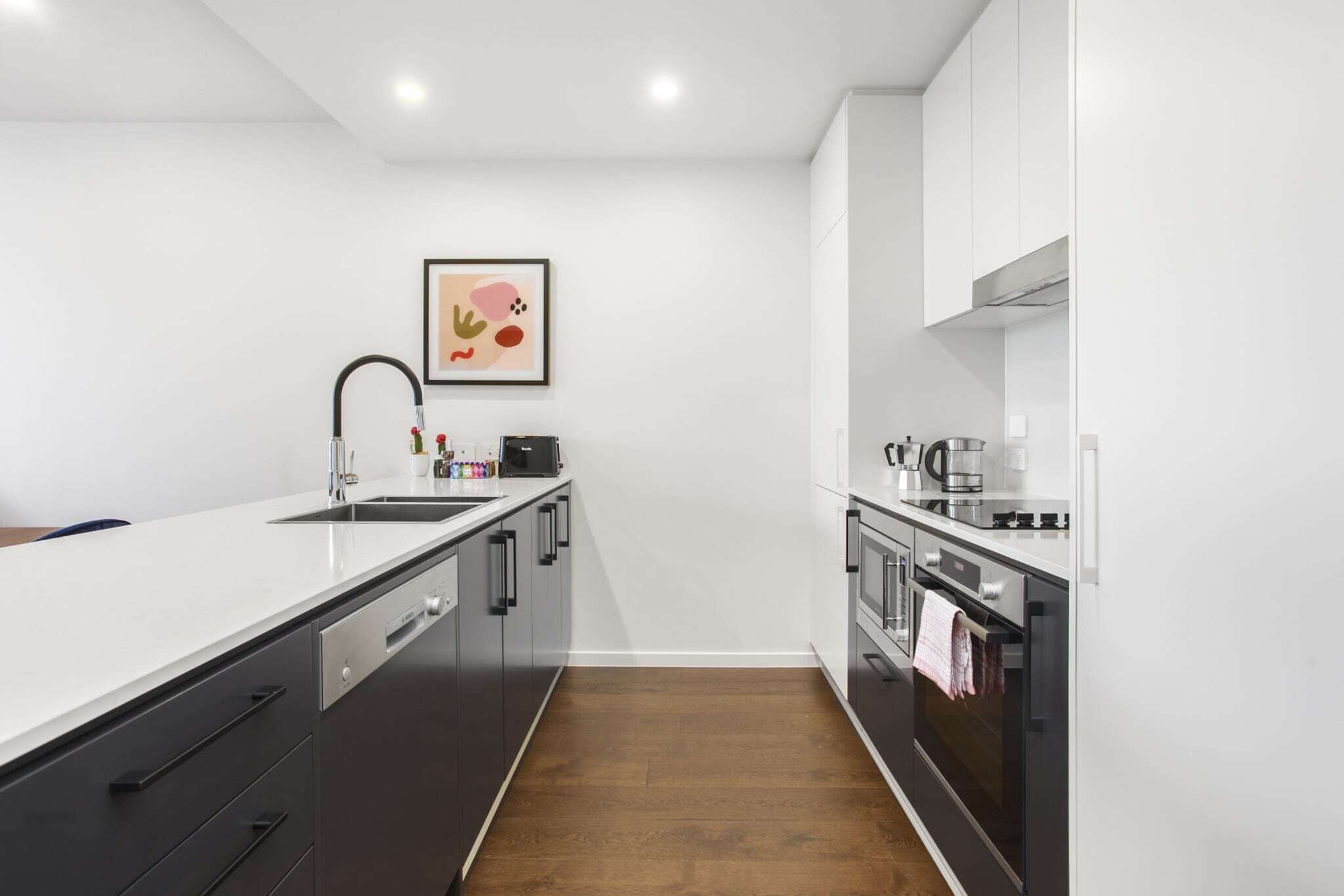 A modern kitchen with a white countertop, black cabinets, a stainless steel sink, and a microwave.