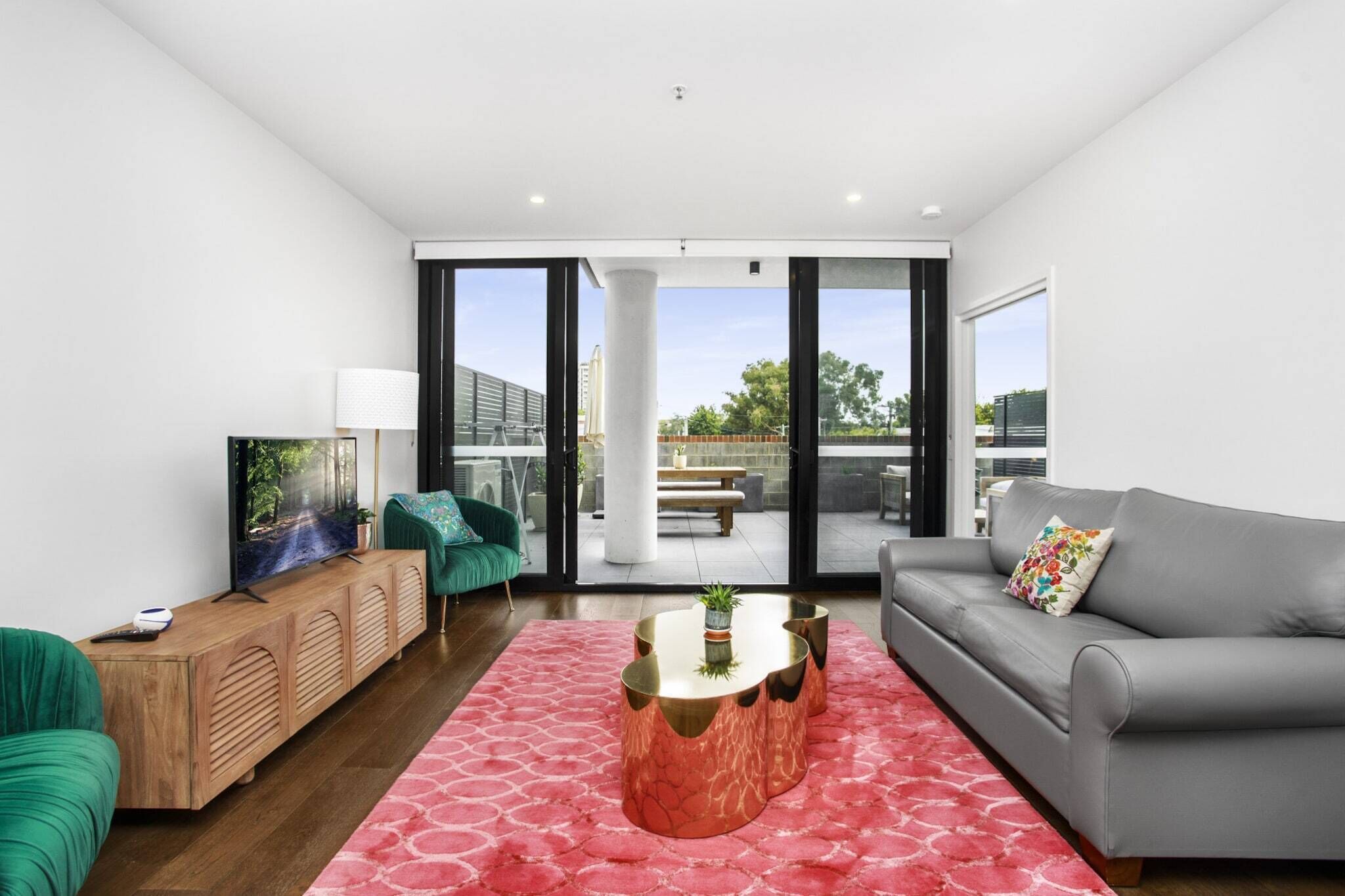 A modern living room with a grey sofa, a green armchair, a wooden console, and a pink rug.