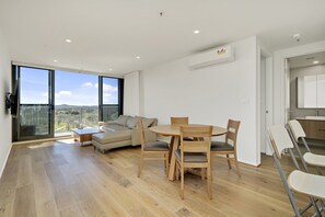 Een moderne woonkamer met een houten eettafel, een beige bank en grote ramen met uitzicht op de stad.