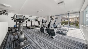 Ein modernes Fitnessstudio mit verschiedenen Cardiogeräten, einem digitalen Display und großen Fenstern mit Blick auf die Stadt.