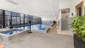 A modern indoor swimming pool area with clear glass walls, a tiled floor, and a shower area. - Executive Unit with Pool and Gym near Riverfront (Southbank)