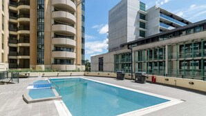 Una piscina en la azotea con agua azul cristalina, rodeada de edificios modernos con balcones y ventanas amplias.