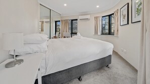 Un dormitorio moderno con una cama grande, una mesita de noche, un espejo y una ventana con cortinas.