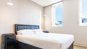 Un dormitorio moderno con cabecera negra, ropa de cama blanca y una mesita de noche con cajones.