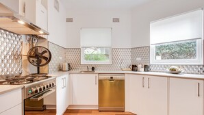 A modern kitchen with white cabinetry, a stainless steel stove, a dishwasher, and a window with a view of greenery. - Art Deco 2-Bed Close to City and Harbour (Neutral Bay)