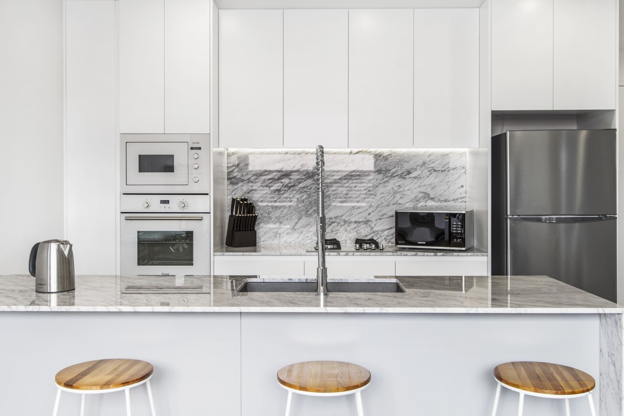 A modern kitchen with white cabinets, a marble backsplash, stainless steel appliances, and a central island with stools.
