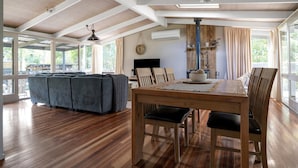 Una habitación amplia con una mesa de madera, sillas y un sofá. Hay un ventanal grande que proporciona luz natural y vistas al exterior.