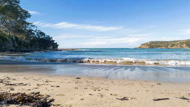 Una playa con aguas azul cristalino, orilla de arena y acantilados rocosos.