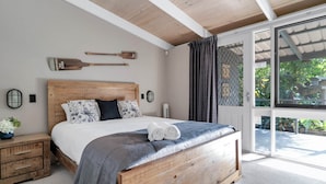 Un dormitorio con una cama de madera, una mesita de noche, una lámpara de pared y un ventanal con cortinas.