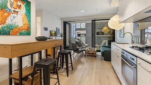 A modern kitchen with a wooden bar, stools, and a large tiger painting. - City View Haven in South Melbourne (South Melbourne)
