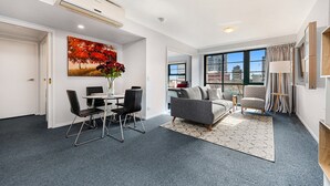 Un salón moderno con un sofá gris, una mesa de comedor con sillas y un amplio ventanal con vistas a la ciudad.