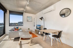 Ein modernes Wohnzimmer mit einer Couch, Sesseln, einem Esstisch, einem Fernseher und einem großen Fenster.