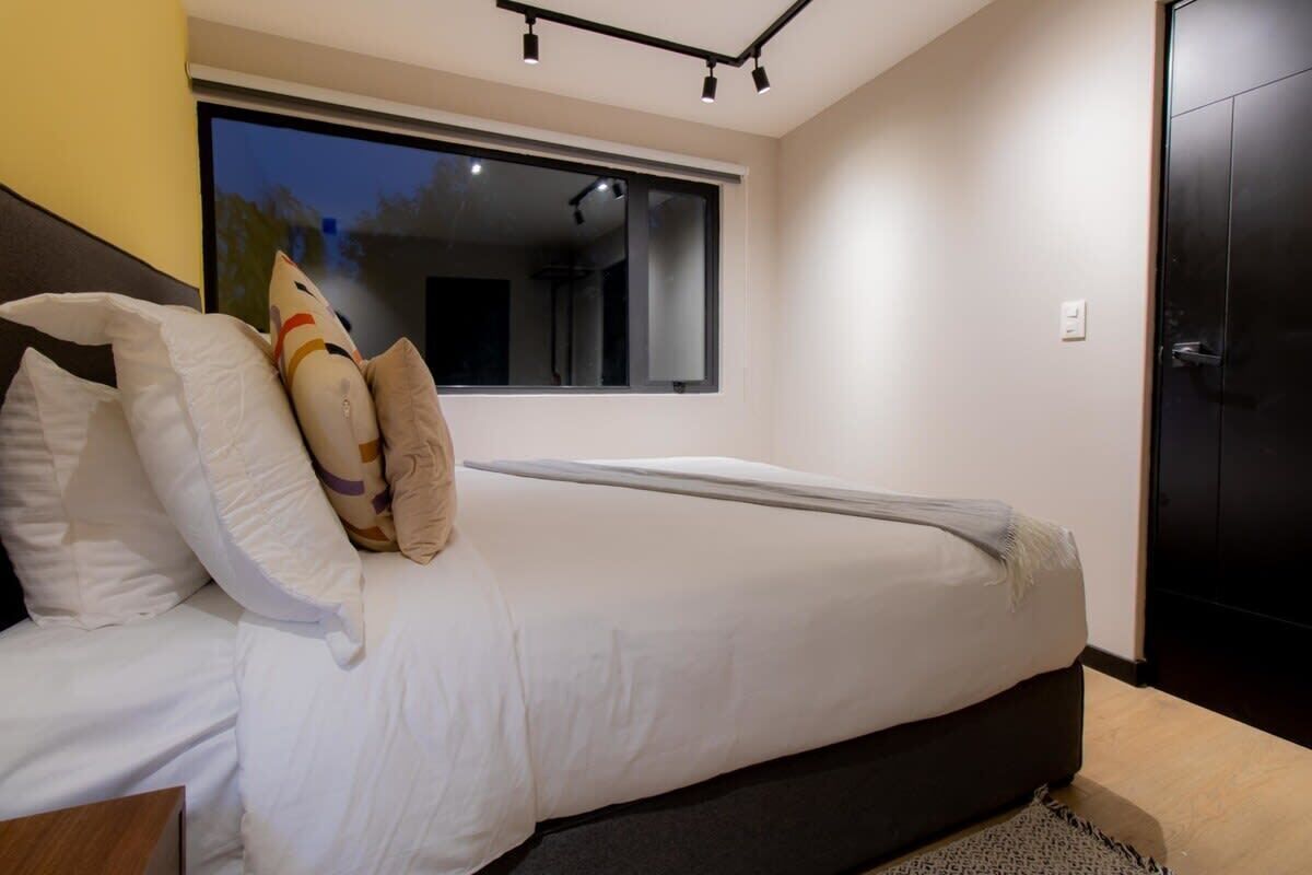 Een slaapkamer met een bed, kussens, een raam en een deur.