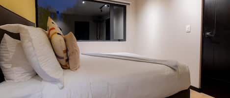 A bedroom with a bed, pillows, a window, and a door.