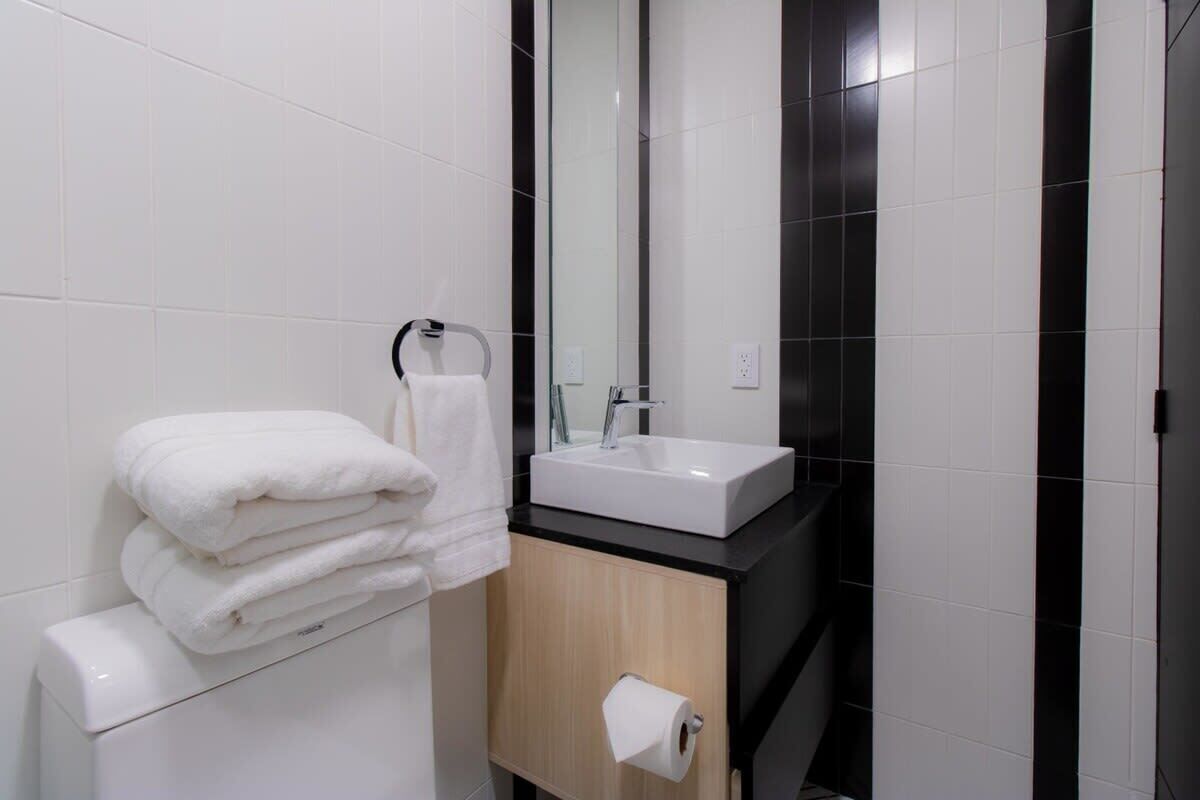 A modern bathroom with white tiles, a black countertop, a white sink, and a wooden cabinet.