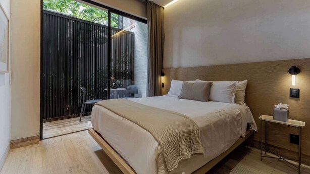 Une chambre moderne avec un grand lit, une table de chevet sur laquelle se trouve une boîte de mouchoirs, et une vue sur un balcon avec une porte coulissante.