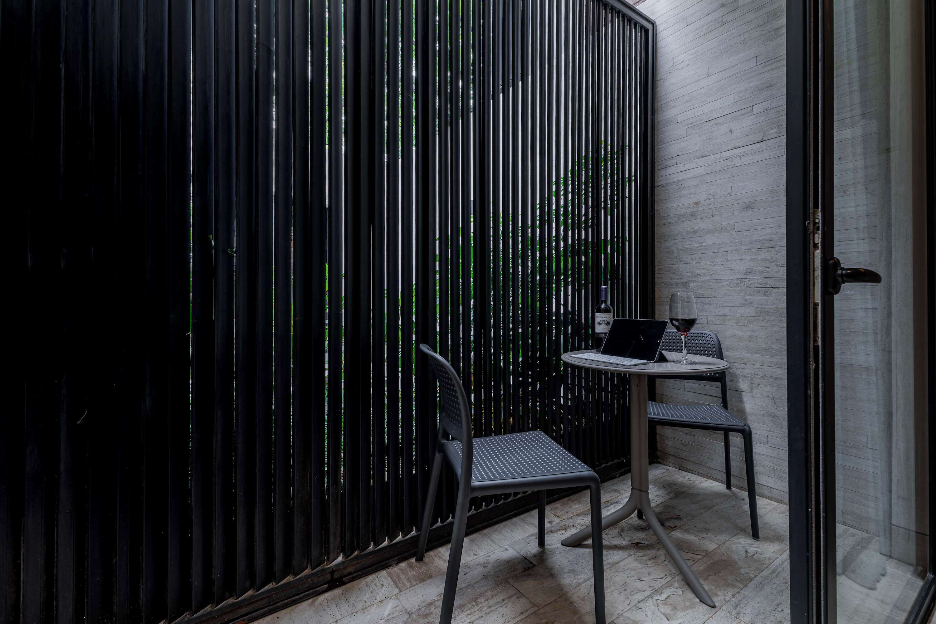A small, modern room with a black metal partition, a small table with a laptop and a glass of wine, and two chairs.