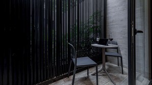 Une petite pièce moderne avec une cloison en métal noir, une petite table sur laquelle se trouve un ordinateur portable et un verre de vin, ainsi que deux chaises.