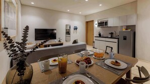 Une chambre d’hôtel moderne dotée d’un coin repas, d’une kitchenette et d’un téléviseur fixé au mur.