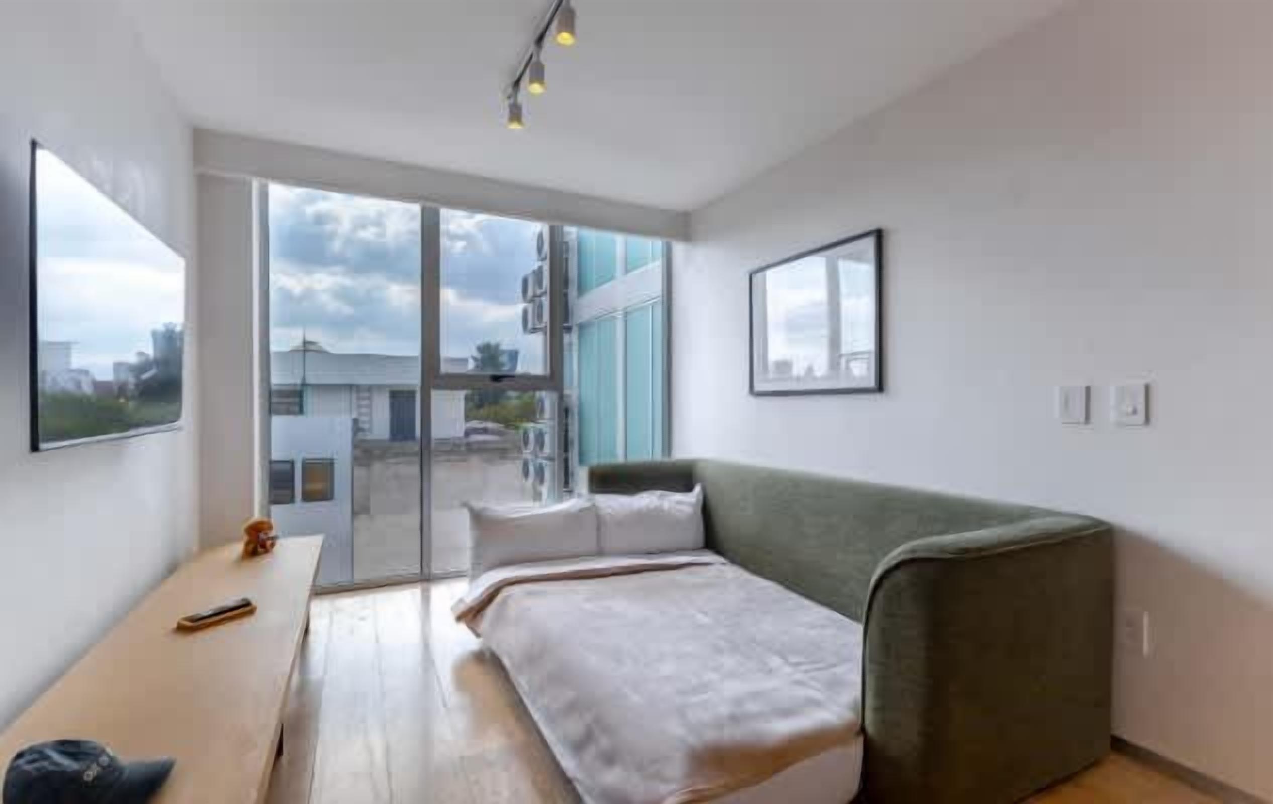 Une chambre moderne avec un lit, un canapé, un bureau et une grande fenêtre.