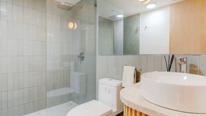 Et moderne badeværelse med en brusekabine i glas, et hvidt toilet og en stor, rund vask.