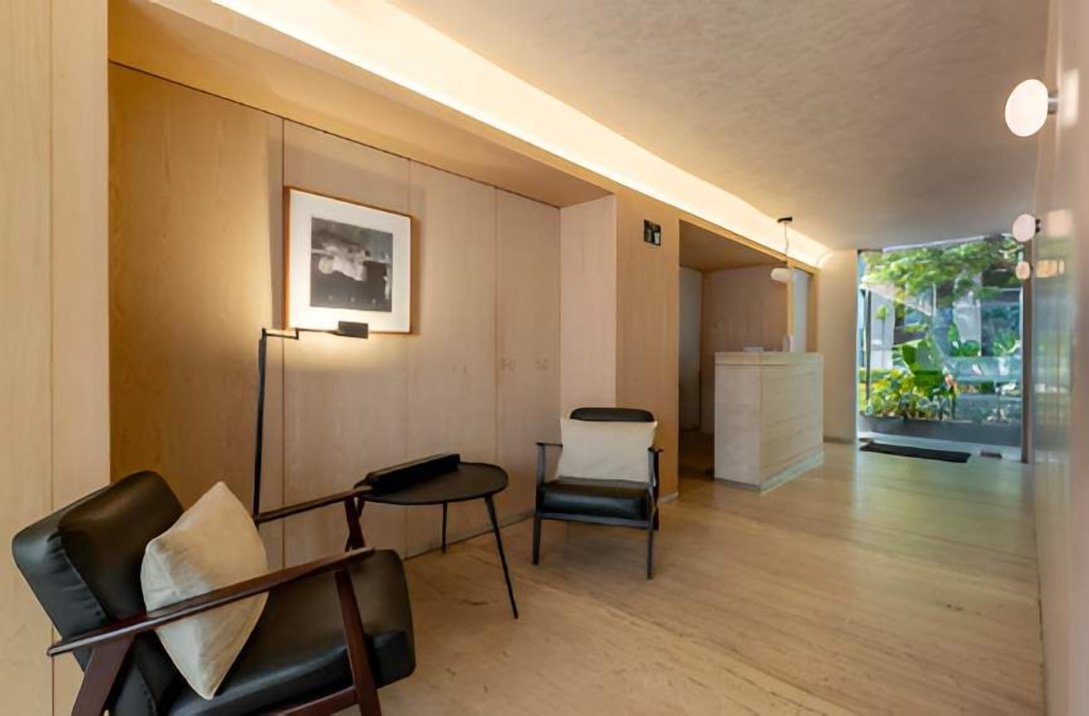 A modern hotel lobby with a reception desk, seating area with two chairs, and a framed picture on the wall.