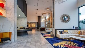 En modern entréhall med ett marmorgolv, en receptionsdisk, en soffa med färgglada kuddar och ett stort fönster med utsikt över staden.