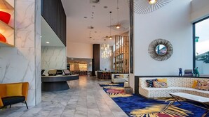 En modern entréhall med ett marmorgolv, en receptionsdisk, en sittgrupp med en mönstrad matta och ett stort fönster med utsikt.