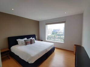Ein modernes Schlafzimmer mit einem großen Bett, einem Nachttisch, einem Fenster mit Blick auf die Stadt und einem Flachbildfernseher.