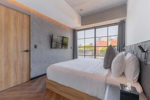 Ein modernes Hotelzimmer mit einem großen Bett, einem an der Wand montierten Fernseher und einem Fenster mit Blick auf Gebäude.