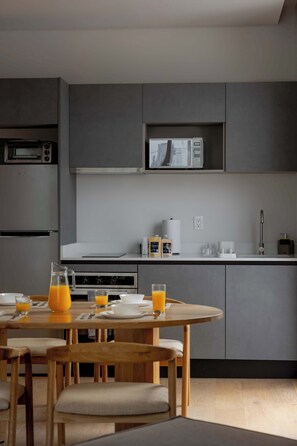 A modern kitchen with grey cabinets, a microwave, and a coffee maker. There is a dining table with chairs and a pitcher of orange juice. - TOP Colonia | Chic 1BR Apartment (Mexico City)