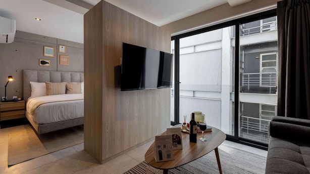 A modern hotel room with a bed, a flat-screen TV mounted on the wall, a coffee table with a menu, and a large window offering a view of the city. - TOP Condesa Loft | Chic Studio (Mexico City)