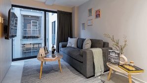 A modern living room with a grey sofa, a small wooden coffee table, and a glass door leading to an outdoor balcony. - TOP Condesa Loft | Chic Studio (Mexico City)