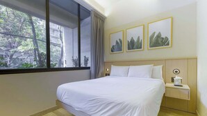 Un llit ben fet a una habitació d'hotel amb una finestra gran, una tauleta de nit amb una làmpada i tres quadres al mur.