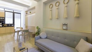 Un saló modern amb un sofà gris, una taula de menjador amb cadires i una cuina al fons.