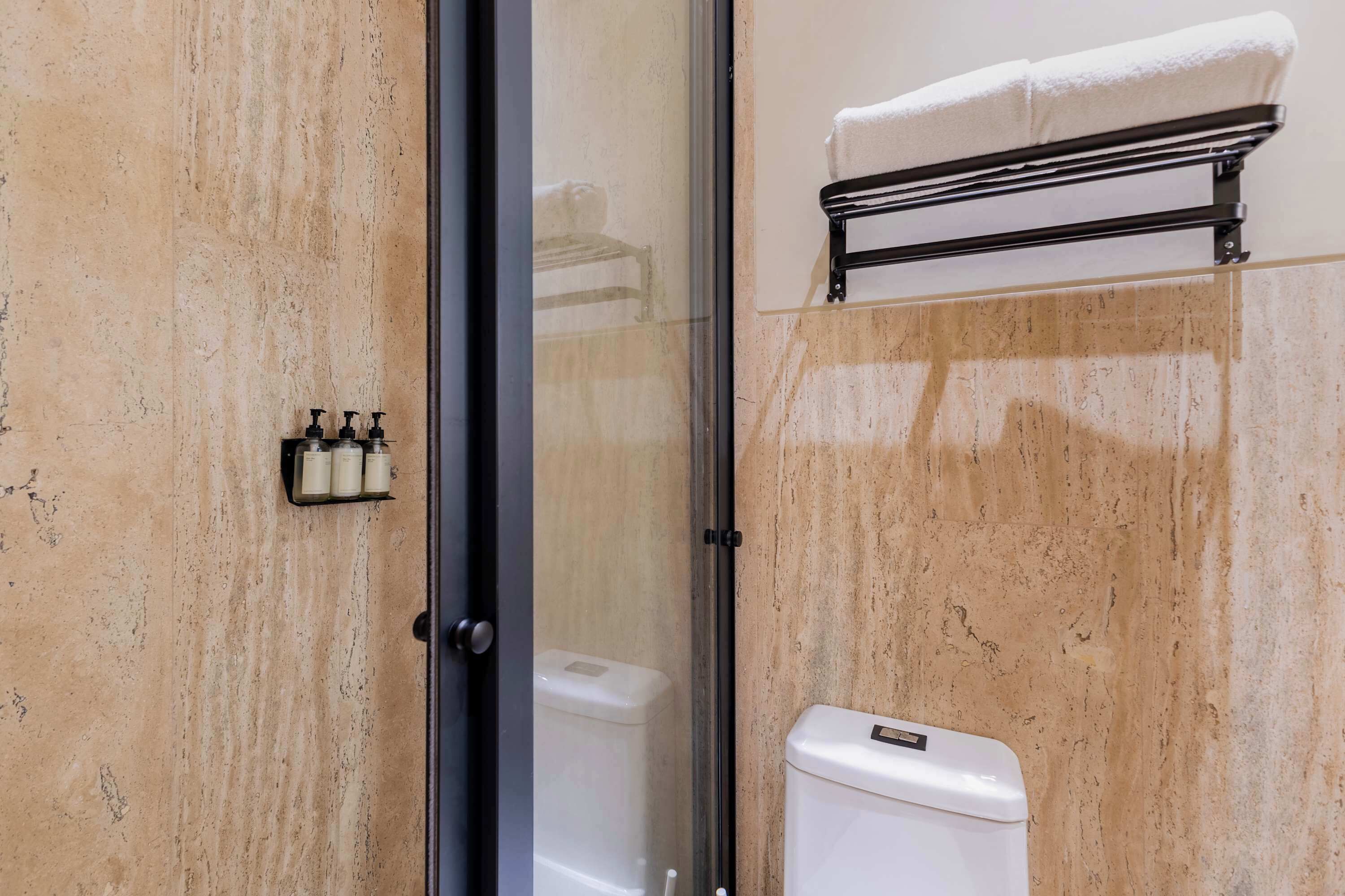 Une salle de bain avec une porte de douche en verre, des toilettes et un porte-serviettes avec une serviette.