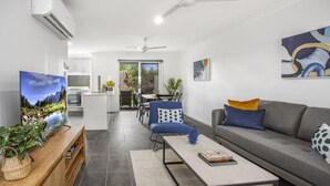 Una sala de estar moderna con un sofá gris, un sillón azul y una mesa de centro. Hay un televisor sobre un mueble de madera y un cuadro en la pared.