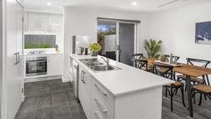 Una cocina moderna con armarios blancos, una isla central con lavamanos y un comedor con mesa y sillas de madera.