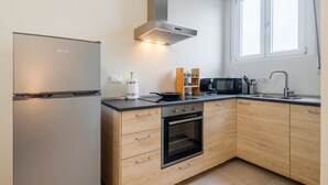 Eine moderne Küche mit Edelstahlkühlschrank, Backofen und Mikrowelle, Holzschränken und einem Fenster für natürliches Licht.
