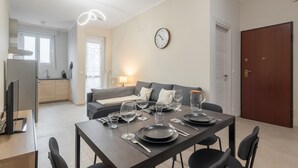 Ein modernes Wohnzimmer mit Esstisch für vier Personen, einer Couch und einer Küchenzeile, sowie einer Uhr an der Wand.
