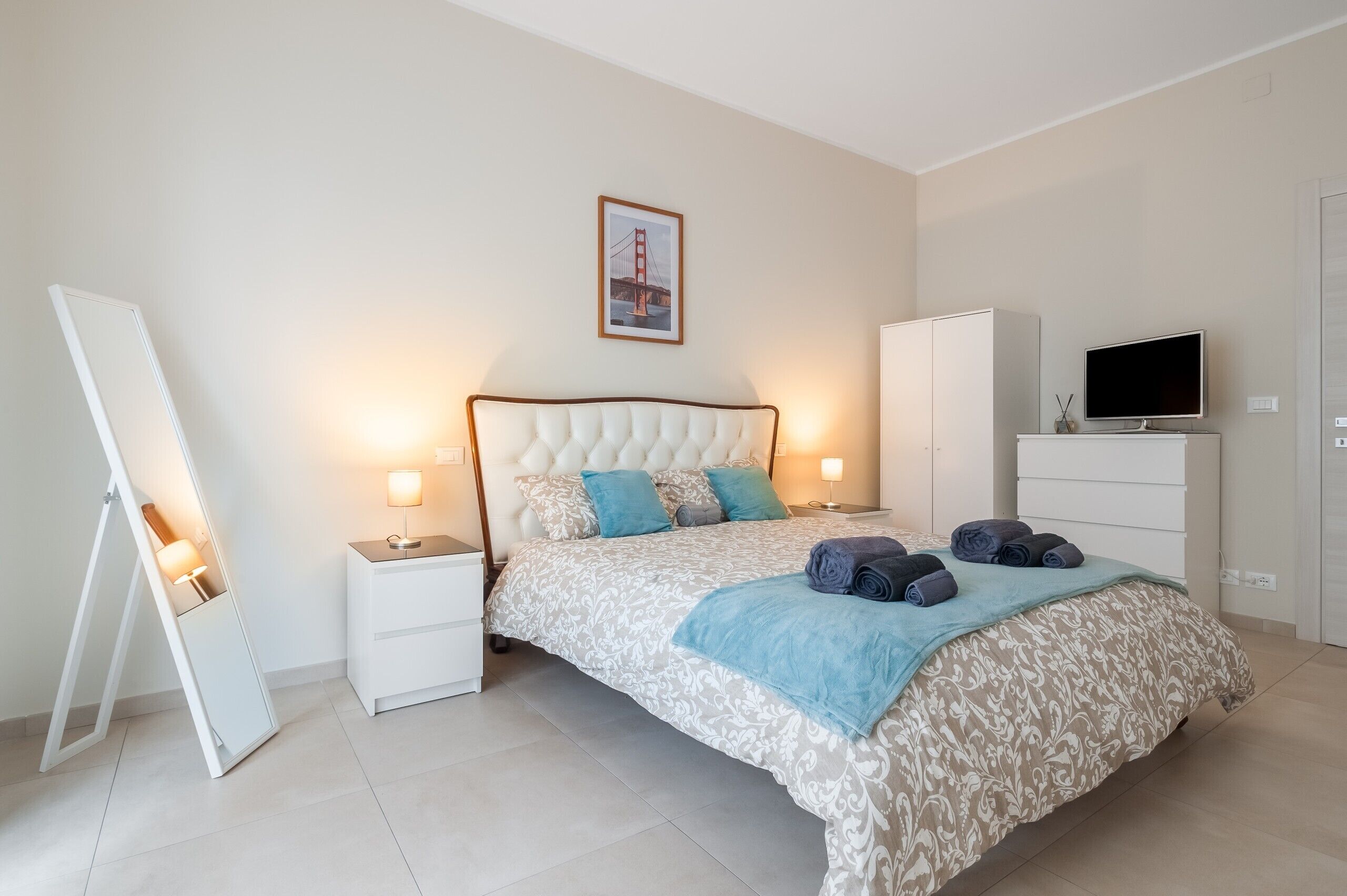 A bedroom with a bed, bedside tables, a TV, a wardrobe, and a framed picture on the wall.