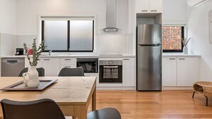 Une cuisine moderne avec des meubles blancs, un réfrigérateur en acier inoxydable et un mur en briques.