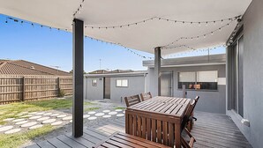 Un espace extérieur aménagé en terrasse, avec une table et des chaises en bois, des guirlandes lumineuses et un coin salon abrité.