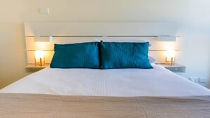 A neatly made bed with a white duvet and two teal pillows, flanked by bedside tables with lamps. - Spacious City Stay Near Lygon Street Dining (Carlton)