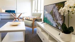 A modern living room with a flat-screen TV, a white table, a comfortable armchair, and a potted plant. - Spacious City Stay Near Lygon Street Dining (Carlton)