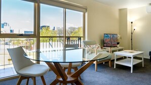 A modern living room with a glass table, two chairs, a TV, and a painting. - Spacious City Stay Near Lygon Street Dining (Carlton)