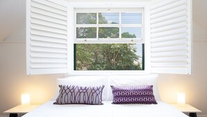 Quarto com uma cama grande, duas luminárias de cabeceira e uma janela com persianas.