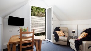Um quarto aconchegante com uma mesa de jantar de madeira, uma cadeira, um sofá e uma televisão fixada na parede.